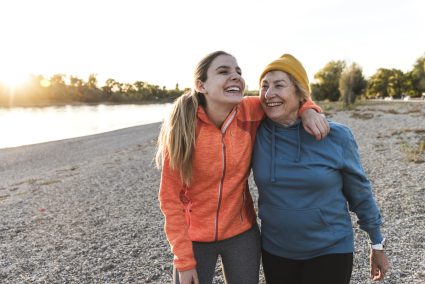 Fit Grandmother And Granddaughter Walking At The River With Arms Around, Having Fun