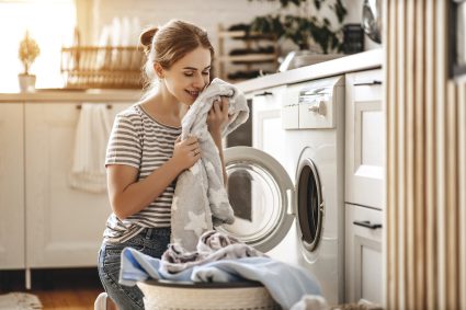 Happy Housewife Woman In Laundry Room With Washing Machine