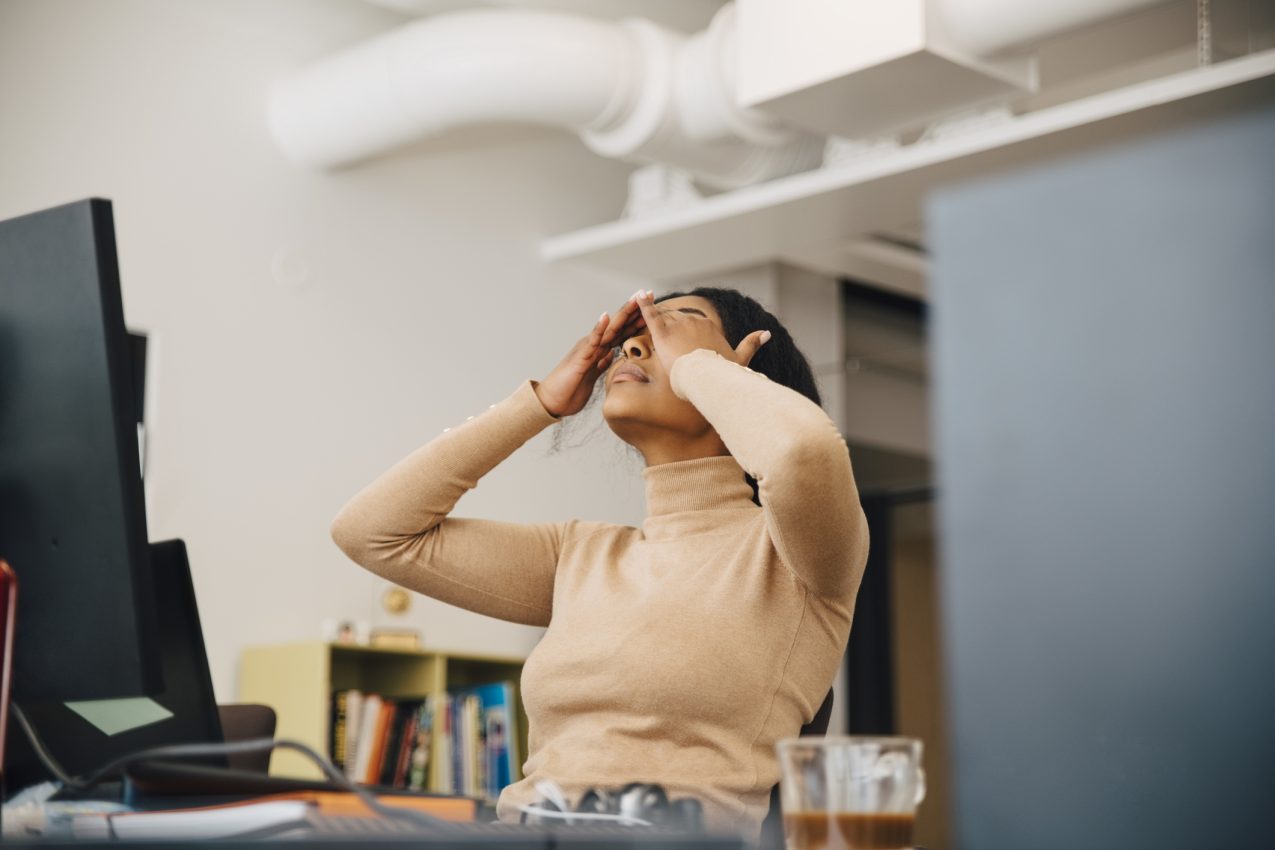 Frustrated Female Computer Programmer With Head In Hands Sitting In Creative Office