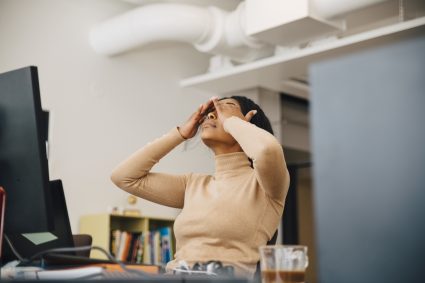 Frustrated Female Computer Programmer With Head In Hands Sitting In Creative Office