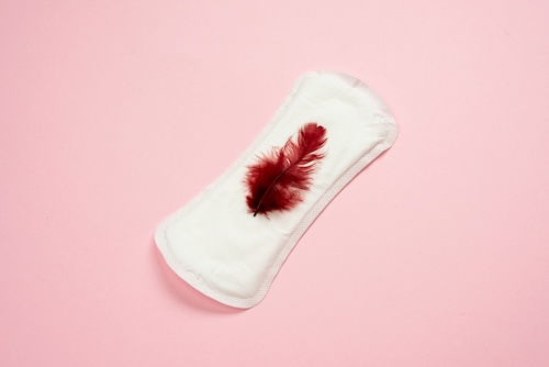 onregelmatig-ongesteld: maandverband met rode veer, roze achtergrond