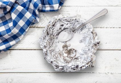Zilver Schoonmaken: een aluminium schaaltje met baking soda en een zilveren lepel en sieraden erin op een witte tafel