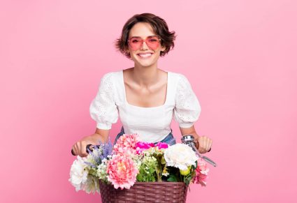 Linnen Looks hema: vrouw op fiets met bloemen in fietsmandje, roze achtergrond