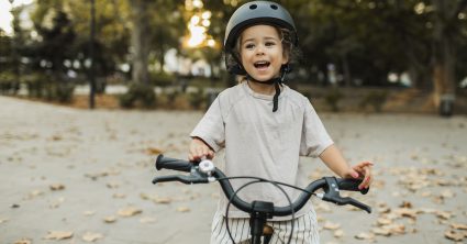Cheerful Child Riding A Bike In Helmet In City Park. Happy Childhood