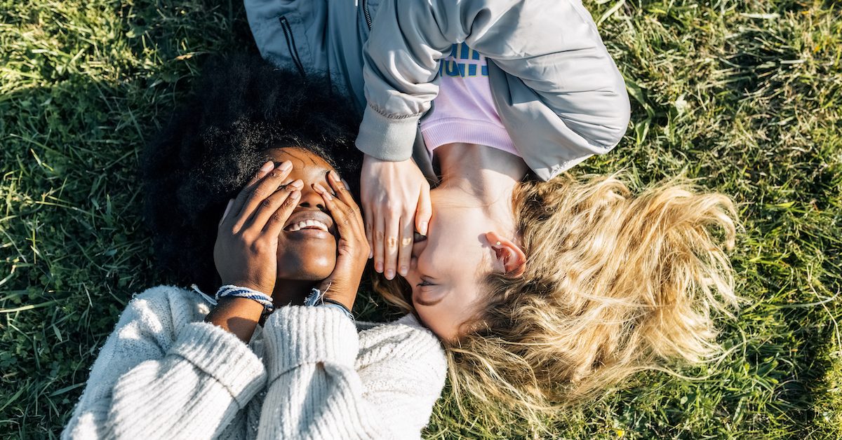 Two Best Friends Telling Secrets Lying In The Grass