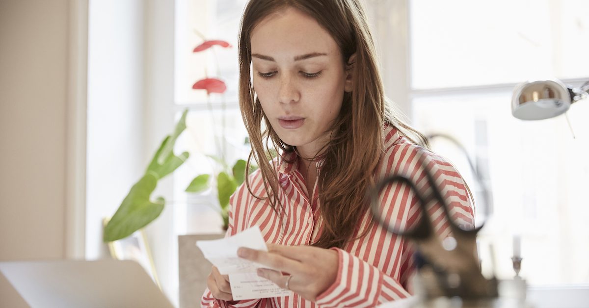 Young Woman Examining Financial Bill While Using Laptop At Home