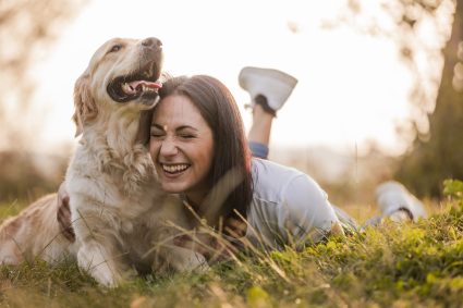 Beautiful Woman Smiling And Cudding Her Dog Lying On The Grass, Lecco, Italy