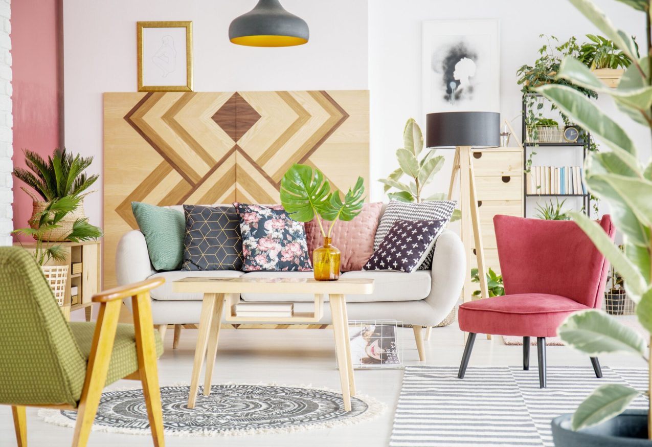 Woonkamer met mix van interieur trends: kleurrijke kussens, houten accenten, veel planten en een retro fauteuil