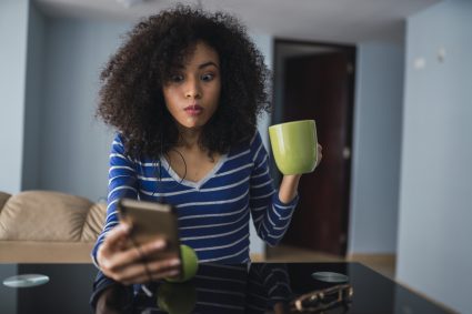 Portrait Of Young Woman With Mug Starring At Cell Phone